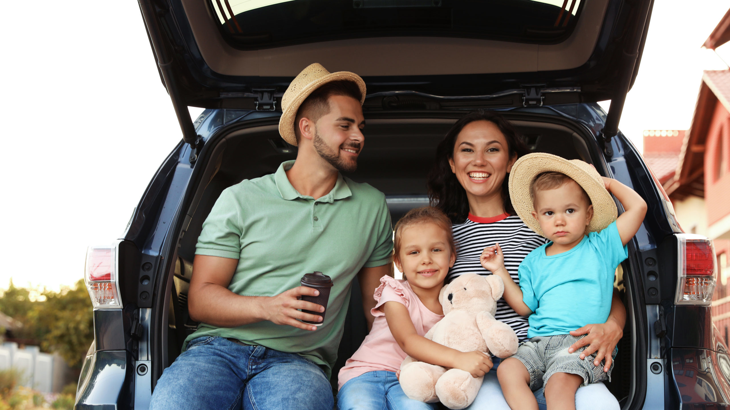 Family of four sitting in the trunk of their car with suitcases nearby